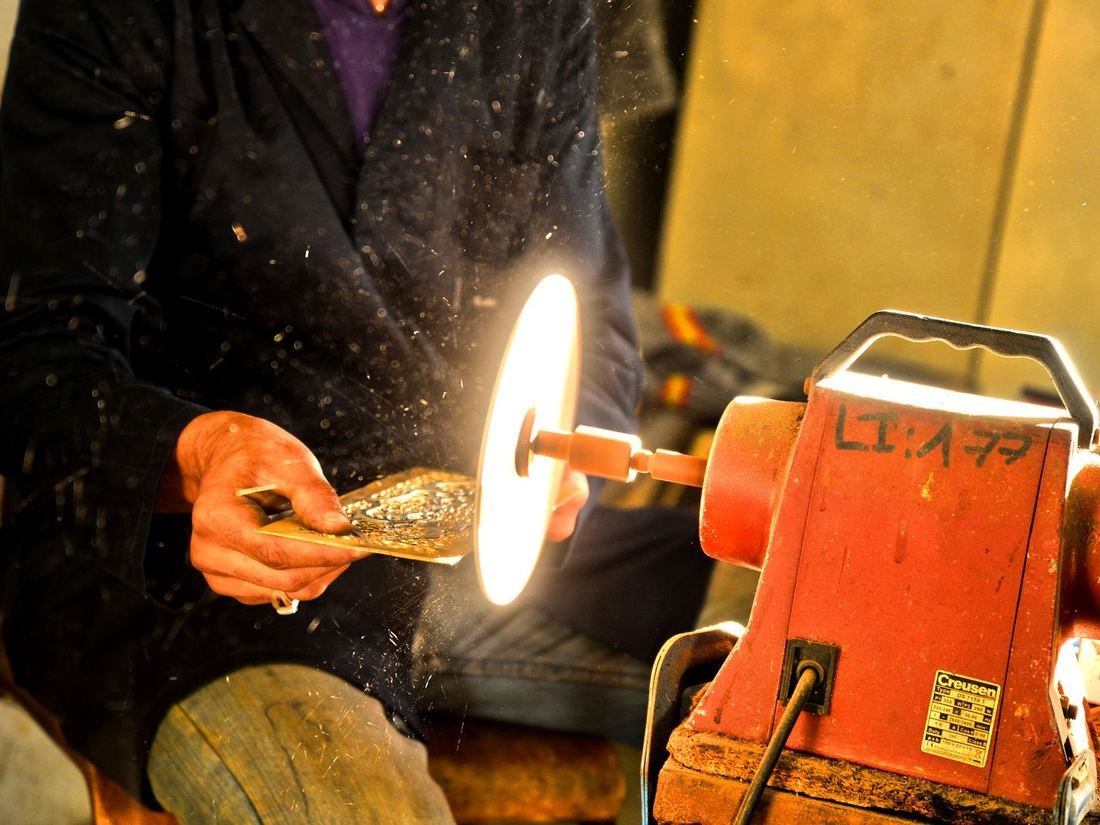 Craftsman polishing a metal piece on a grinding wheel in a workshop
