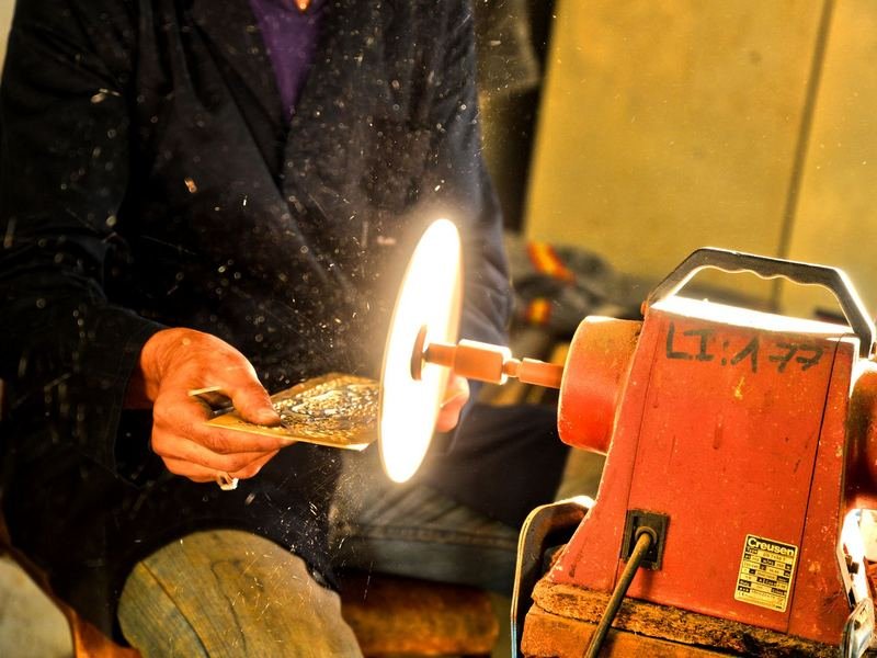 Craftsman finishing a metal piece on a grinding wheel